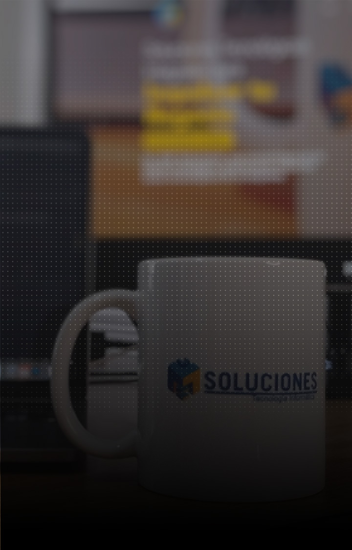 Imagen de una taza con logotipo de JMC Soluciones sobre un escritorio con computadoras de fondo